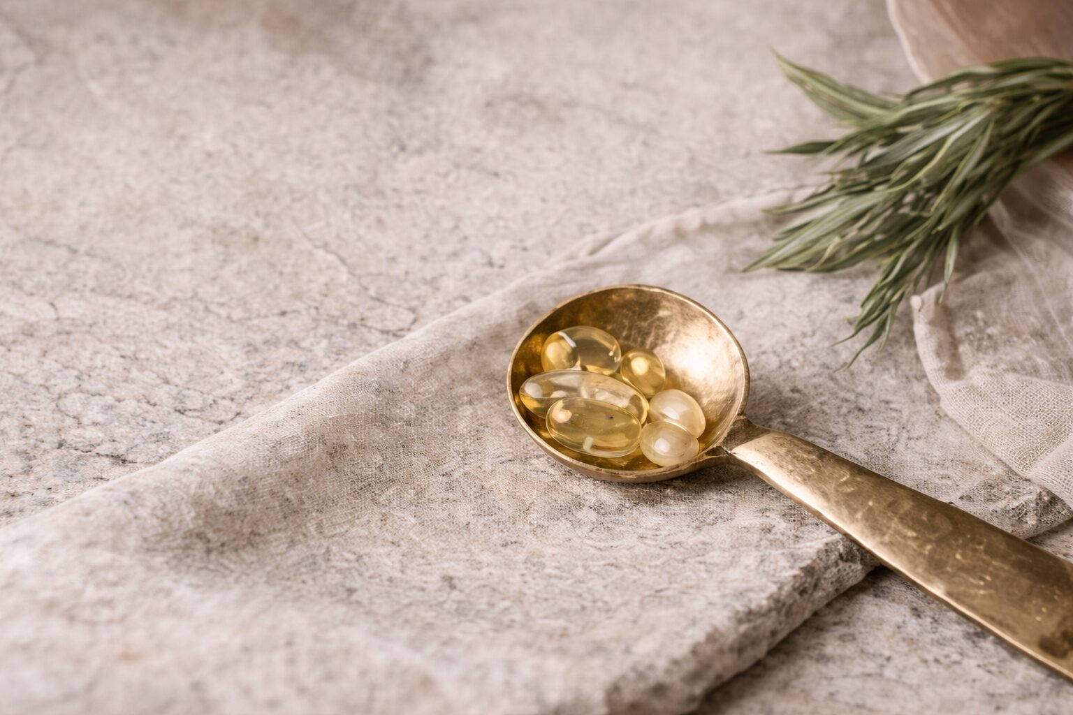 Golden liquid and capsules in a vintage spoon on textured surface.