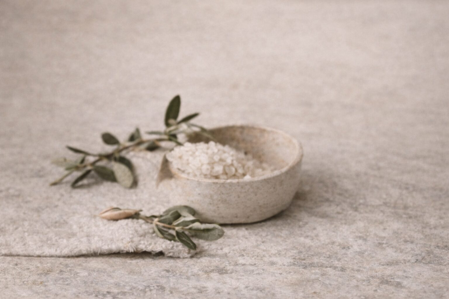 A bowl of white powder with green leaves on a neutral surface.